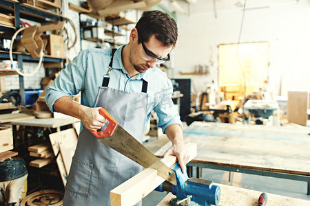 熟练木匠锯一块木头放置在工作台副与手锯在他的车间