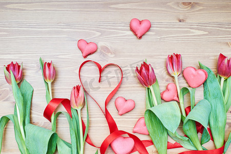 实物鲜花花束摄影照片_在木桌上放着鲜花和丝带的心形马卡龙。情人节创意装饰
