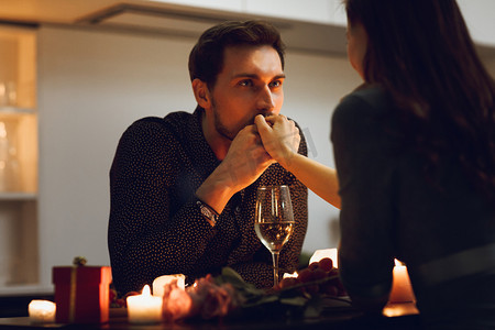 美丽的激情夫妇有一个浪漫的烛光晚餐在家里, 男人亲吻手