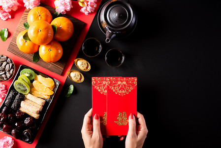 中国新年装饰品。 女性手拿着便盆或红包，橙色和金色的锭纹在黑色的石头背景上。 汉字