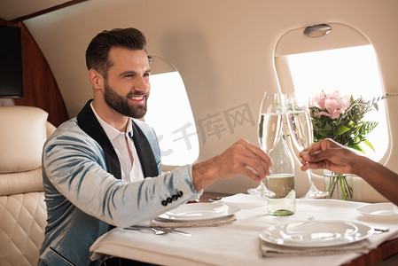 在私人飞机上，非洲裔美国妇女与优雅男子在餐桌边碰杯香槟酒的部分景象