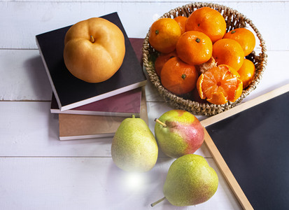 orange摄影照片_Group of orange fruit put in woven basket,beside blurred Chinese pear,on white timber board,blurry light around
