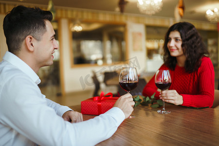 love摄影照片_Young couple having a romantic dinner and toasting with cups of red wine. Sweet couple celebrate their anniversary. Valentines day celebration concept. Relationship, surprise and love concept.