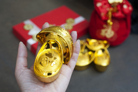 中国金锭手头上有汉字，意为隐身、富有、黄金、好运、健康。 礼品盒和红包为背景. 中国新年礼物的概念.