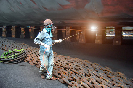 worker, paint man, working for repainting after sand blasting of the bottom layer of the commercial ship in floating dock yard by spraying paint machine