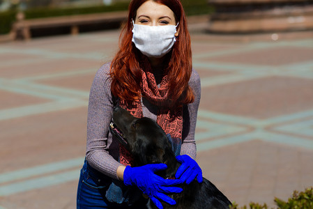年轻的女性使用面罩作为防止与她的狗一起散步的验尸官。全球COVID大流行病概念图像.