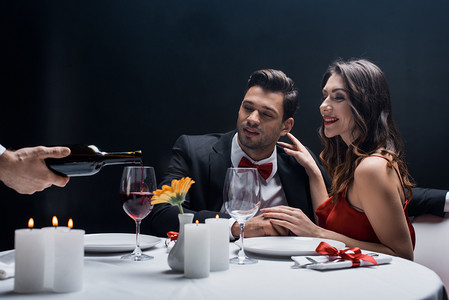 2爱情摄影照片_侍应生把葡萄酒倒入玻璃杯中，与雅致的夫妇在与黑人隔离的餐桌旁享用