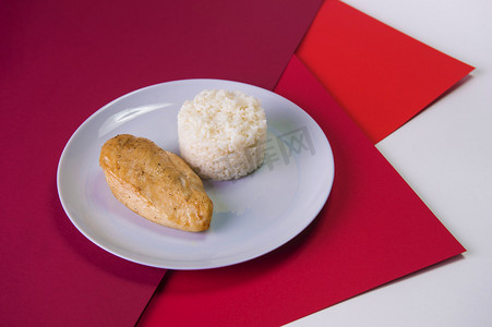 配以煮过的白米的灰盘烤鸡肉片的侧视图。色彩艳丽的红色背景下的早餐。主菜和副菜放在一个盘子里.