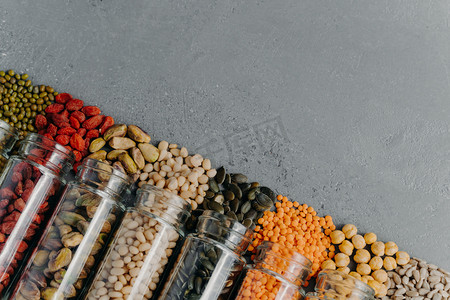 goji摄影照片_Zero waste. Organic grains in glass jars. Pumpkin seeds, chickpea, mung beans, lentils, goji berry, pistachio, sun seeds spilled from bottles. Copy space at upper right corner