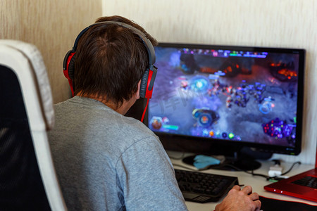 虚拟现实现实摄影照片_在耳机使用电脑在家里玩游戏的集中年轻玩家的背部视图。计算机游戏竞赛游戏控制对抗概念
