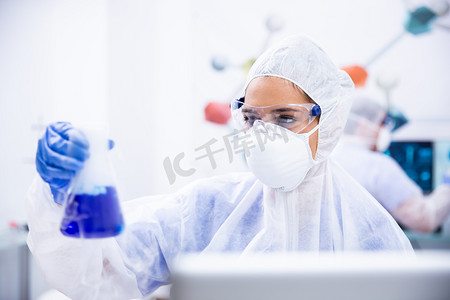 戴护目镜和手套面罩的化学家拿着一个装有蓝色液体的容器.