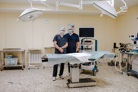 两名医生在白色手术室里手挽手，头戴医用工作服，头戴便帽.