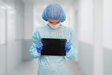 身着防护服的女医生：医疗面罩、帽子和长袍。这名妇女使用数字平板电脑，并在屏幕上显示疾病统计数据.