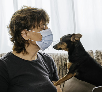女人坐在客厅里，戴着口罩，抵御考罗奈德、眼镜蛇或任何其他疾病，惊讶地嗅着她的狗