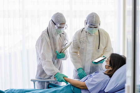 疾病防疫摄影照片_身穿防护服和戴口罩的男医生和女医生正在检查疾病控制区女病人的症状。COVID患者的护理和治疗概念19.