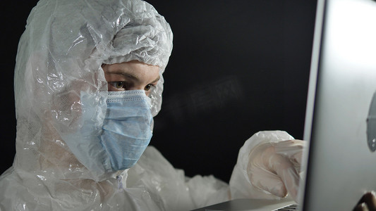 身穿白衣戴口罩的科学家医生在黑色背景特写上小心地打开笔记本电脑