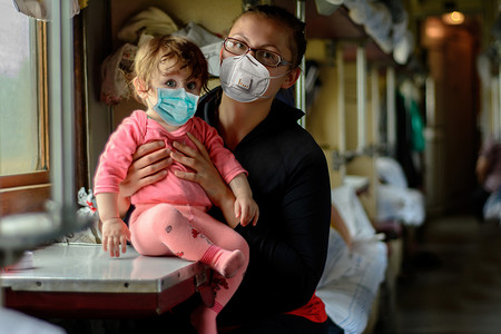 欧洲铁路运输在检疫和验尸报告大流行后恢复。戴着医疗面具的妈妈和小女儿坐2021年的火车旅行.