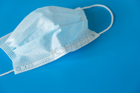 一种典型的三层医疗外科口罩，用蓝色背景盖住口鼻。防止细菌和大肠埃希菌的概念