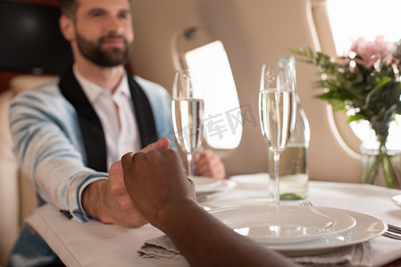 在私人飞机上与非洲裔美国女人牵着手就餐的快乐而优雅的男人的选择性焦点