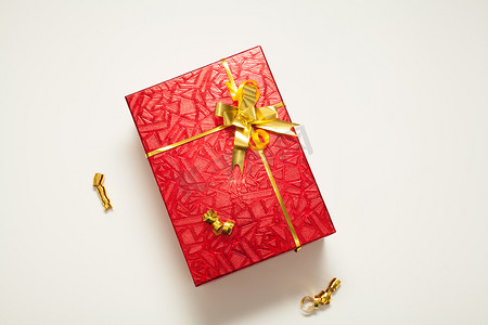 金色缎带缎带摄影照片_礼盒红色，闪烁着金色的蝴蝶结，装饰着金色的缎带和圣诞球，白色的背景上，有一个地方刻有题词。 新年或圣诞节的概念礼物.