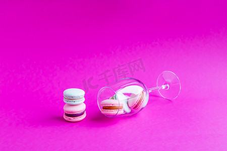 简约饼干摄影照片_马卡龙法国饼干在一个玻璃高脚杯粉红背景。 简约的概念。 复制空间.