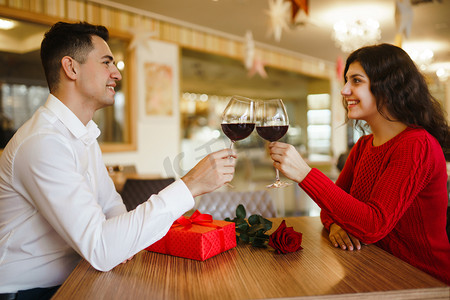 Young couple having a romantic dinner and toasting with cups of red wine. Sweet couple celebrate their anniversary. Valentines day celebration concept. Relationship, surprise and love concept.