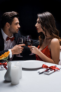 相亲相爱的摄影照片_两对优雅的情侣彼此凝视着对方，在被黑色隔离的餐桌旁与葡萄酒相亲相爱的侧视图