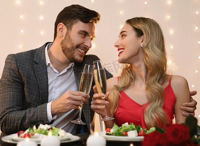 年轻的情侣们在餐馆里享受浪漫的夜晚，在酒杯中倒入香槟