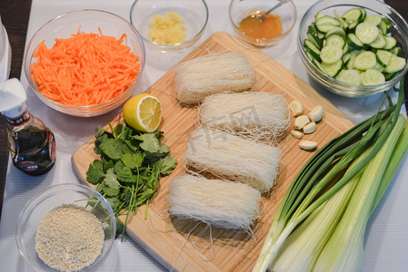 亚洲菜材料︰ 玻璃面条、 黄瓜、 胡萝卜、 酱油、 芝麻、 大蒜、 生姜、 芹菜、 香菜、 葱切木板上.