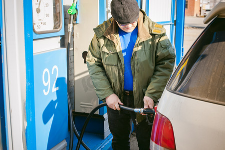 加油站矢量摄影照片_男子在一个加油站填充车辆油箱燃料。成年男子与一个小胡子和眼镜，加油前长途旅行的道路上向非网络加油站汽车