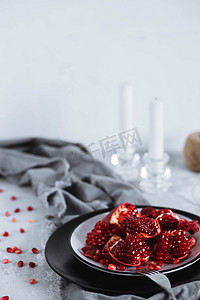 装饰精美的桌子。红色成熟的石榴果实在一个黑色的盘子上的灰色桌子上的蜡烛。健康食品、水果和蔬菜概念