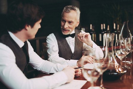 诚邀品鉴摄影照片_Experienced sommelier makes notes about taste qualities of wine drink sitting in restaurant.