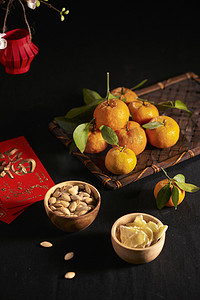 越南新年摄影照片_黑色表面上的农历新年传统小吃和新鲜的柑橘碗