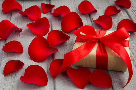 礼品盒与红色丝带和玫瑰花瓣在灰色木制背景