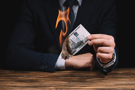 裁剪拍摄的商人燃烧俄罗斯卢布钞票以上的木桌 