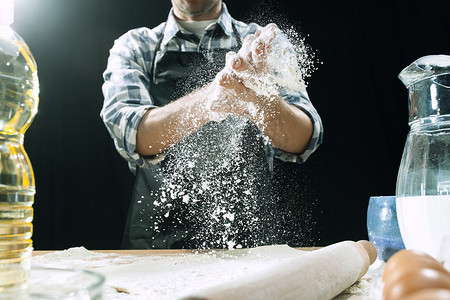 厨师面团摄影照片_专业的男性厨师在厨房的桌子上洒面团和面粉、预贴或烤面包