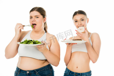 苗条的女人吃甜甜圈, 而超重的妇女吃绿色菠菜叶隔离在白色