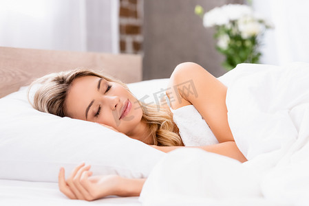 pajamas摄影照片_Young woman in pajamas sleeping on white bedding at home 