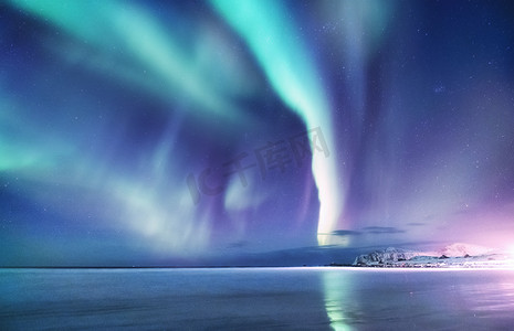 与水背景摄影照片_罗弗敦群岛上的北极极光, 挪威。山上的绿色北极光。夜空中的极地灯光。夜间冬季景观与极光和倒影在水面上。自然背景在挪威