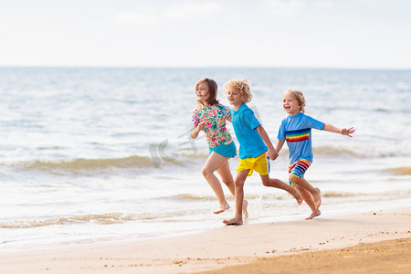 孩子们在热带海滩玩耍。孩子们在暑假时在海上游泳和玩耍。沙子和水的乐趣，防晒幼儿。小男孩和小女孩在海滨跑来跑去.