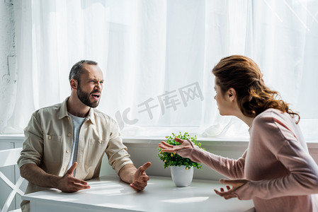 选择性的焦点愤怒的男人手势和看女人，而坐在家里 