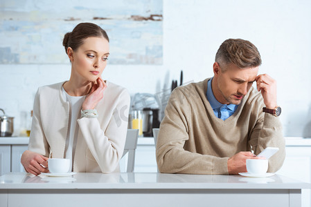 小家电直通车背景摄影照片_dissatisfied man using smartphone and ignoring woman during breakfast in kitchen