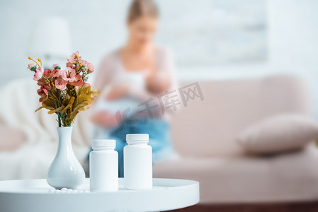 节日热点摄影照片_容器与药丸, 花在花瓶和母亲母乳喂养婴儿在家里后面