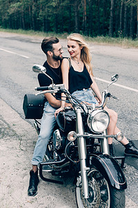 电单车司机摄影照片_幸福的年轻夫妇骑自行车的人坐在绿色森林附近的黑色摩托车