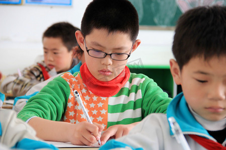 2013年4月25日，在中国东部山东省文登市一所小学上课时，一名戴眼镜的中国学生正在写字。
