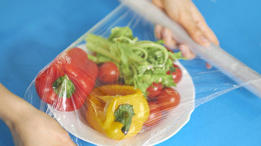 女人用食品膜把食物贮存在白桌上.包装产品用透明聚乙烯食品膜辊.