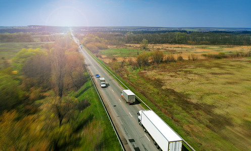 Transport logistics background with trucks on a highway between fields