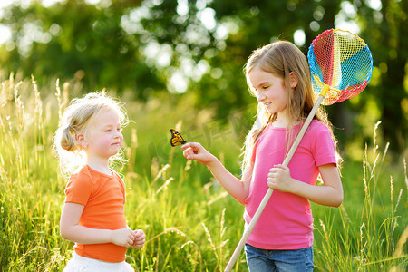 两个小姐妹用勺子网捉蝴蝶和虫子。在阳光明媚的夏日探索大自然的孩子们.
