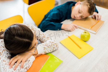 在图书馆里, 疲惫的小学生在与书籍的桌子上睡觉的眼镜的高角度的看法  