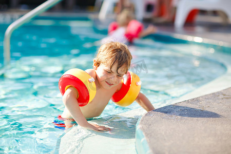 快乐的小男孩在游泳池里玩得很开心。积极快乐健康学龄前儿童学习游泳。与安全的浮雕或游泳。家庭, 假期, 夏天的概念